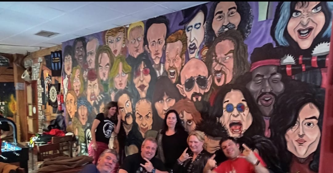 Un grupo frente a un mural que celebra a leyendas del heavy metal.